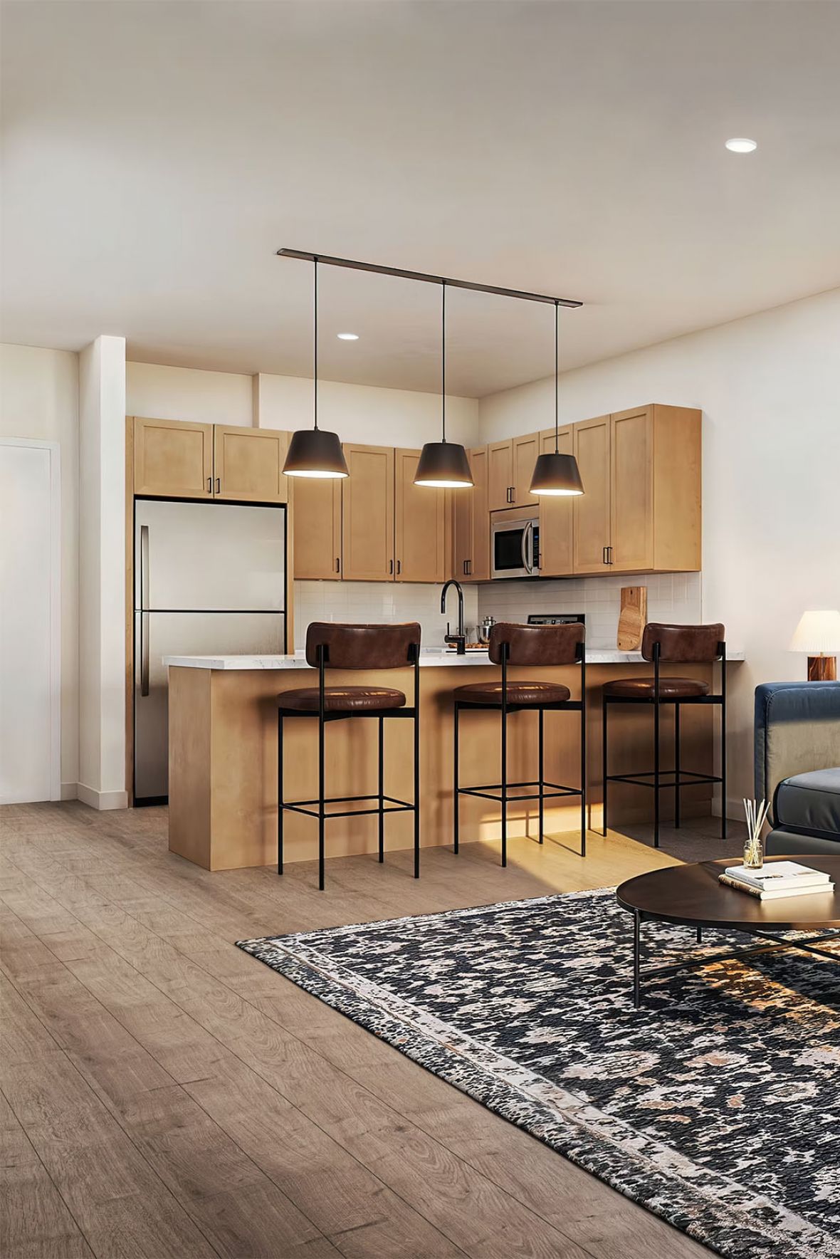 Modern open-concept living room and kitchen with a blue sofa, armchair, and a patterned rug.